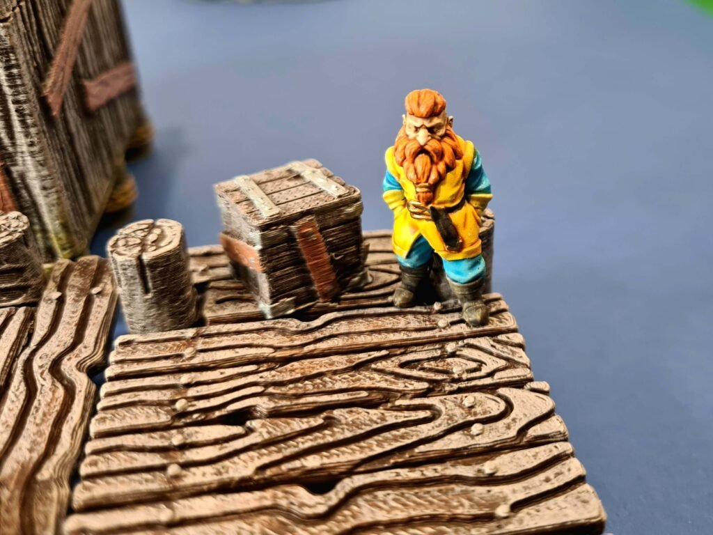 Figurine de nain marchand peinte à la main sur un quai en bois miniature, décor de port en impression 3D pour JDR, caisses de transport détaillées, Les Trésors du Donjon.