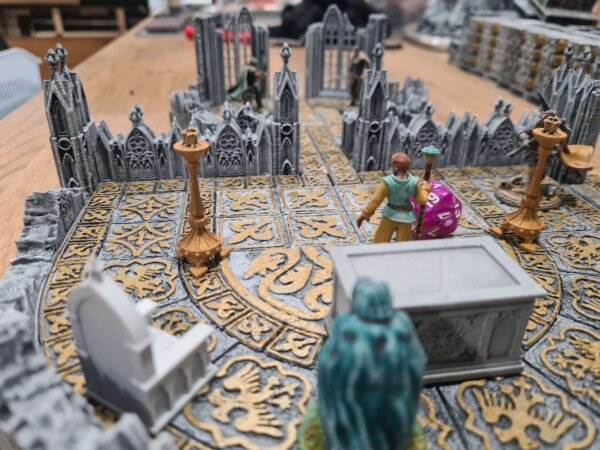Donjon JDR sur mesure — arène gothique en jeu avec figurines, chandeliers dorés et dé D20 violet