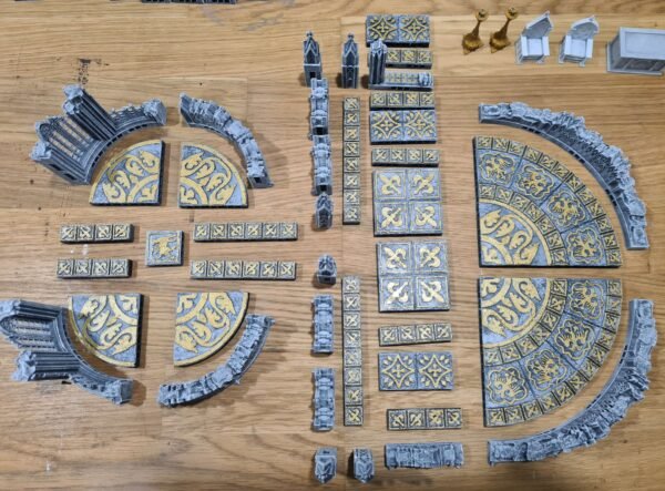 Donjon JDR sur mesure — pièces étalées avant assemblage : dalles ornementales dorées, arches et colonnes PLA+