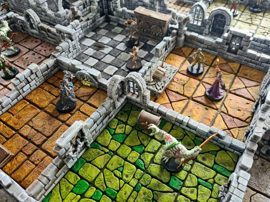 Vue aérienne d'un donjon 3D modulaire montrant différentes salles avec dalles vertes, ocres et grises, incluant du mobilier et des figurines.