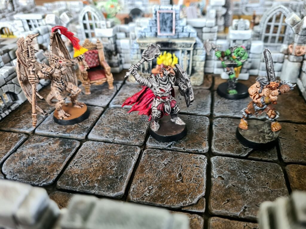 Scène de combat entre un barbare, un guerrier du chaos et un démon ailé sur un plateau de jeu 3D modulaire.